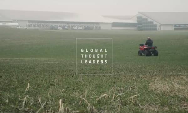 Dairy farmer driving an ATV through a field behind freestall barns.